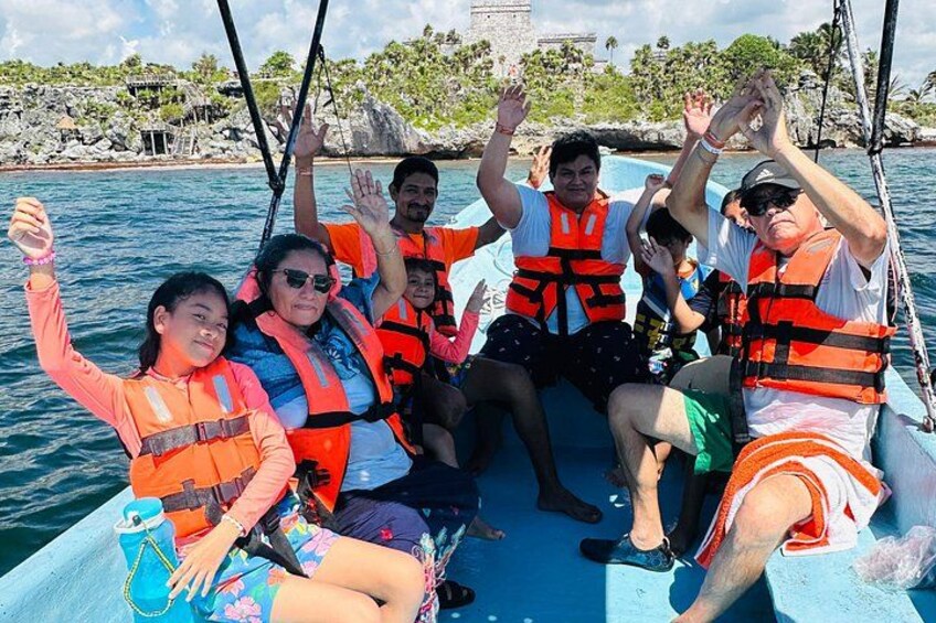 A group of people on a boat wearing life jackets, with a rocky shoreline and palm trees in the background. 4