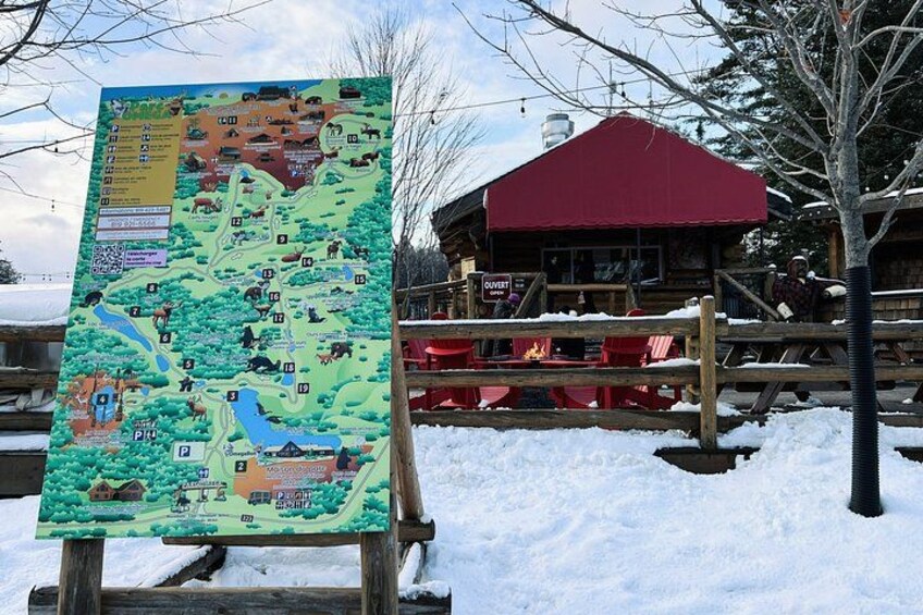 A snow-covered outdoor area with a wooden signboard displaying a map and a red-roofed building. 5