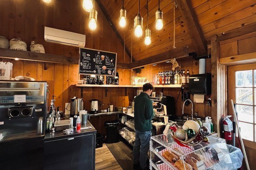 A rustic café interior with wooden walls, hanging light bulbs, a coffee machine, and a person preparing drinks. 4