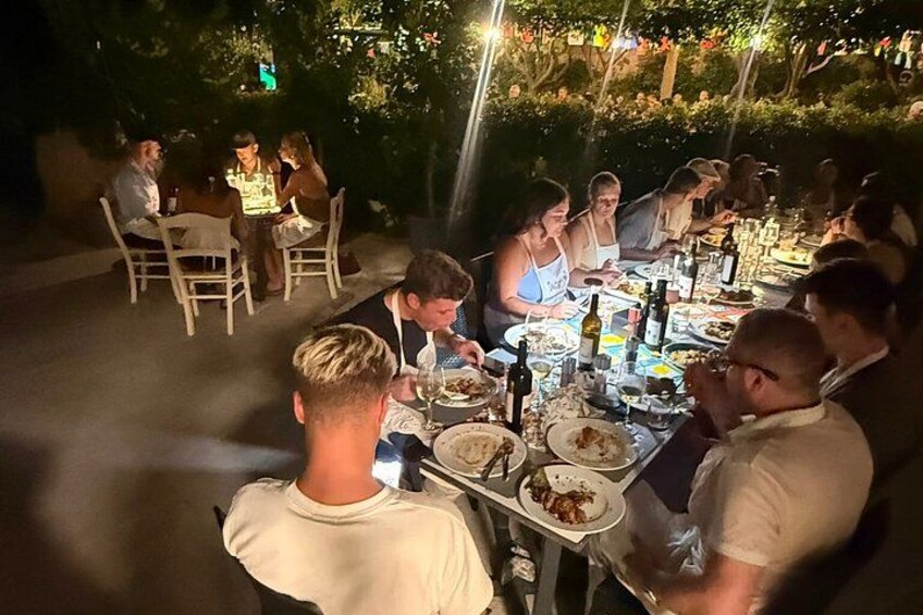 A group of people dining outdoors at night with tables set up and illuminated by string lights. 2