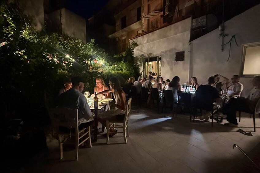 An outdoor dining area with tables and chairs, surrounded by greenery and buildings. 3