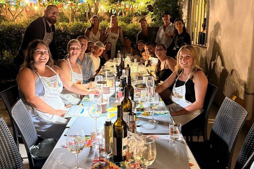 A group of people seated at an outdoor dining table with wine glasses and bottles. 5