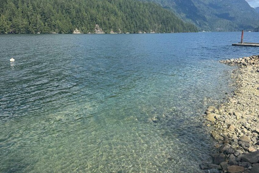 A clear lake with a rocky shoreline and forested mountains in the background. 2
