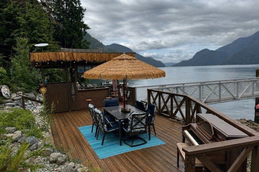 A wooden deck with a table and chairs, a thatched umbrella, and a view of a lake and mountains. 4