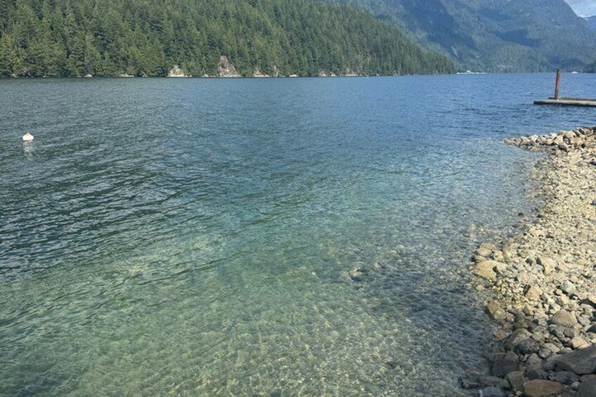 A clear lake with a rocky shoreline and forested mountains in the background. 5