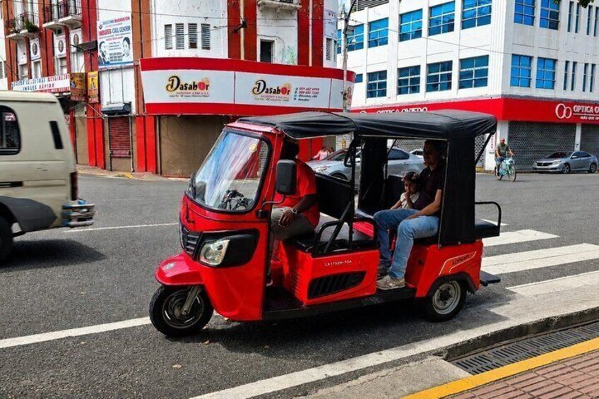 A red auto-rickshaw on a city street with buildings in the background. 4