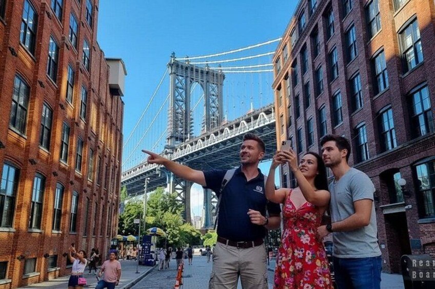 A group of people taking a selfie with the Brooklyn Bridge in the background. 1