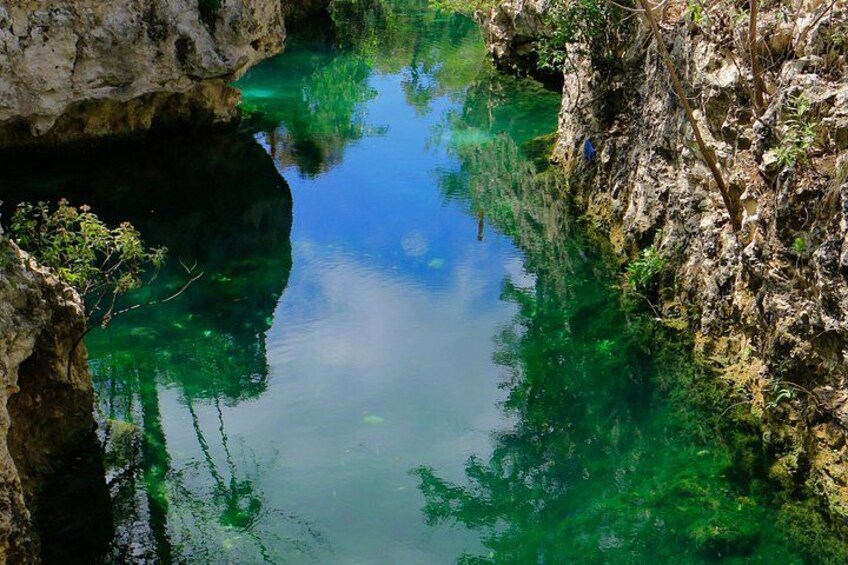 A clear blue water body surrounded by rocky cliffs and sparse vegetation. 3