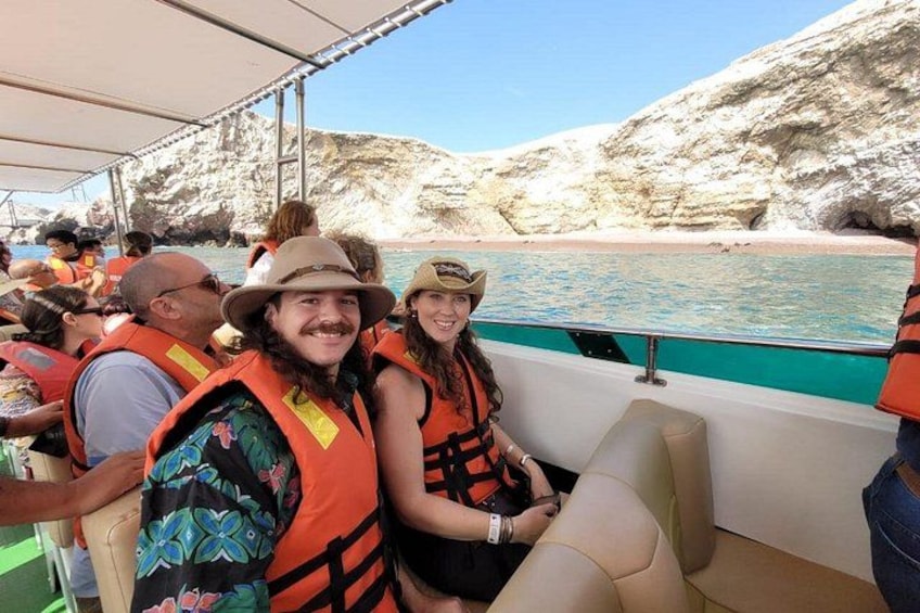 People on a boat wearing life jackets, rocky cliffs, and a beach in the background. 2