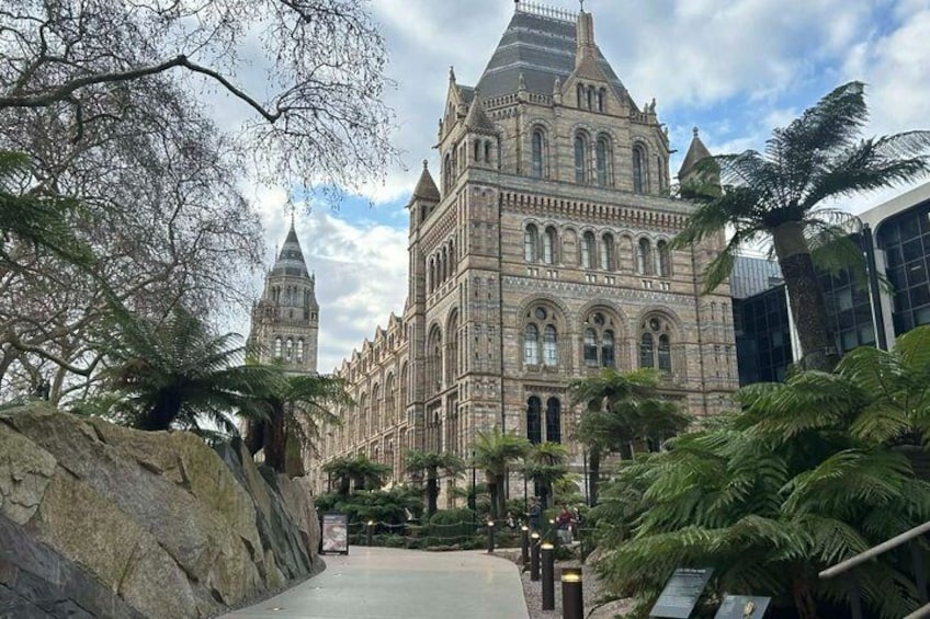 A historic building with arched windows and a pointed roof, surrounded by tropical plants and a large rock. 4