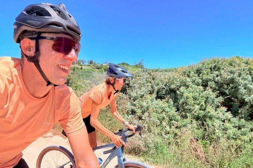 Two cyclists on a trail with dense shrubbery and a clear blue sky. 1