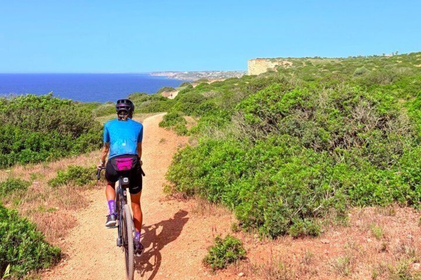 A cyclist on a dirt path with a coastal landscape in the background. 3