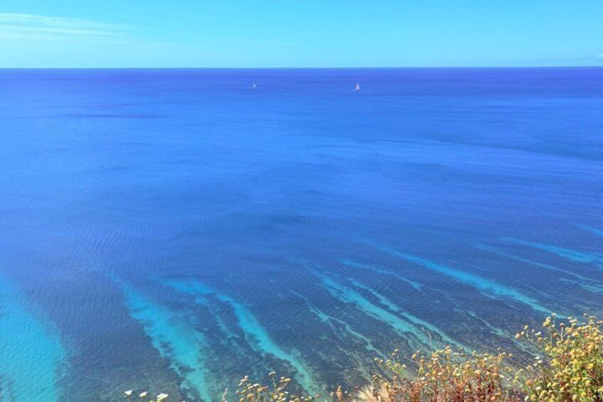 A clear blue ocean with visible underwater structures and a distant sailboat. 5