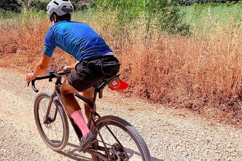 A person riding a bicycle on a gravel path with dry grass on the sides. 5