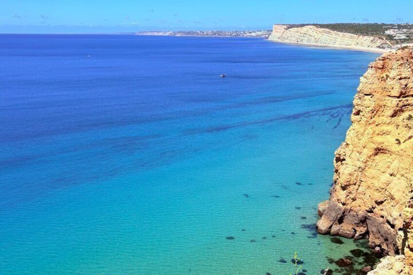 A coastal landscape with clear blue waters, rocky cliffs, and a distant shoreline. 4