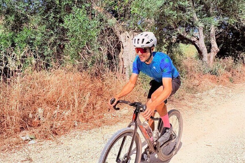 A person riding a bicycle on a dirt path surrounded by dry grass and trees. 2