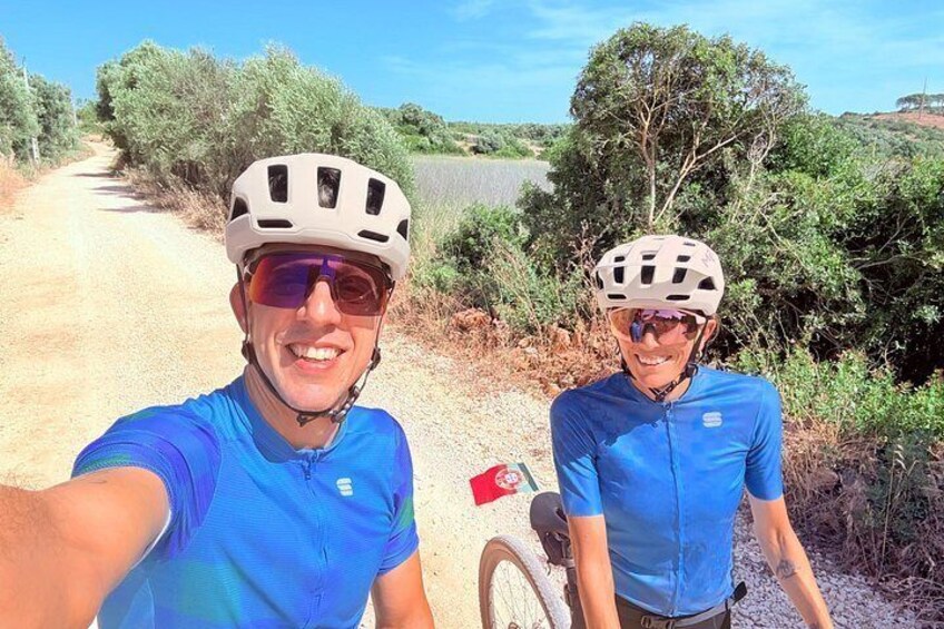 Two cyclists on a dirt path with trees and a clear sky. 3