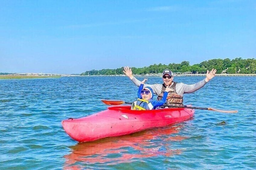 A person in a red kayak on calm water with a clear sky and a distant shoreline. 5