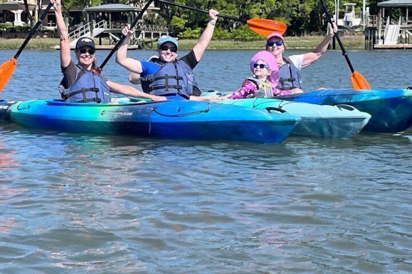 Three people kayaking on a calm lake, wearing life jackets and paddling with oars. 2
