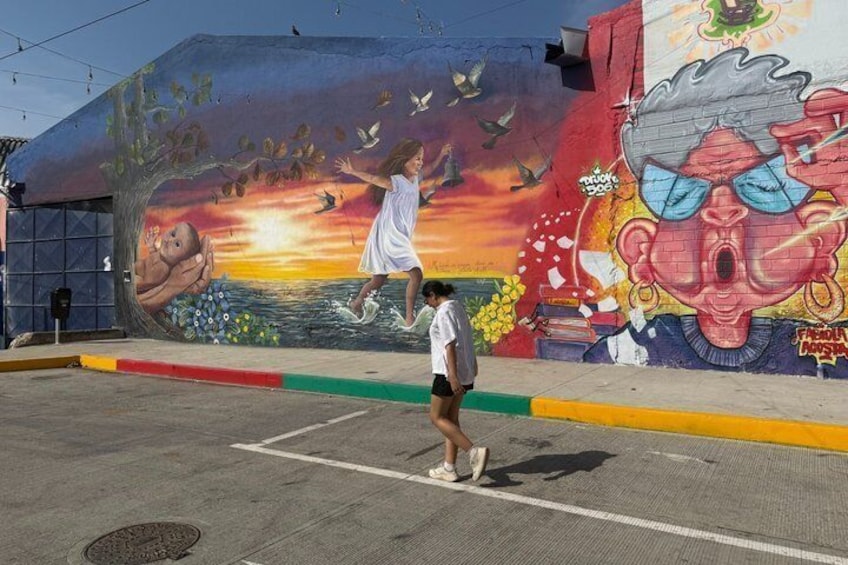 A mural with a girl jumping, a sunset, and a man with sunglasses. 5