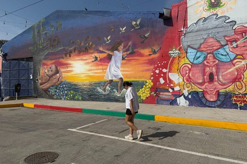 A mural with a girl jumping, a sunset, and a man with sunglasses. 4