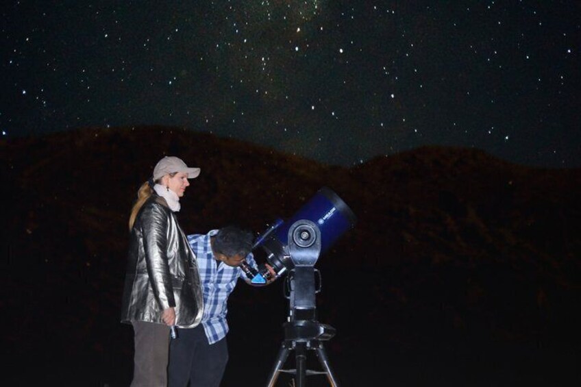 Two people using a telescope under a starry night sky. 1