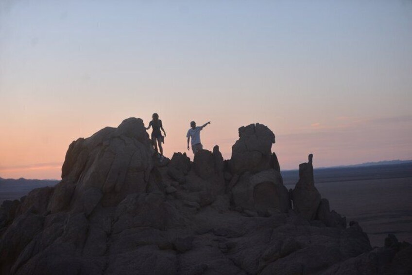 Two people hiking on rocky terrain with a sunset in the background. 2