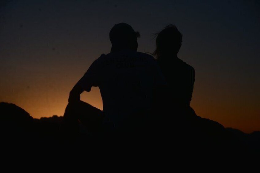 Two people sitting on a rock with a sunset in the background. 3
