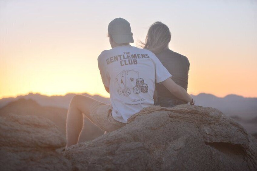 Two people sitting on a rock with a sunset in the background. 4