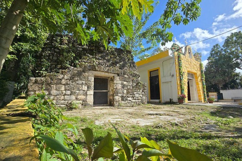 A stone building with a yellow door, surrounded by greenery and a small pond. 4