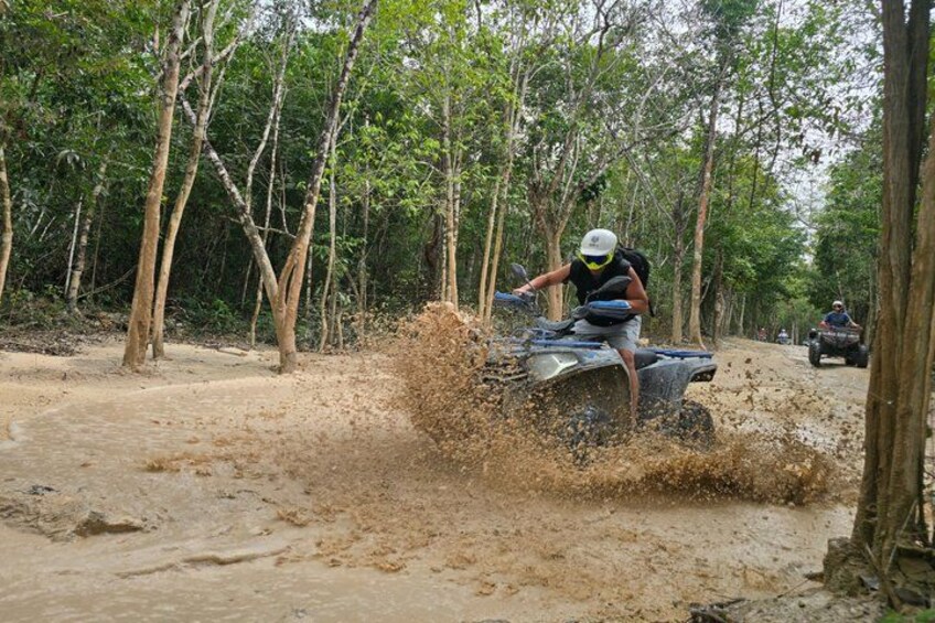 A person riding an ATV on a muddy path surrounded by trees. 1