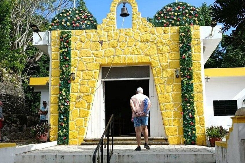 A stone building with a bell tower, decorated with flowers, and a person standing at the entrance. 4