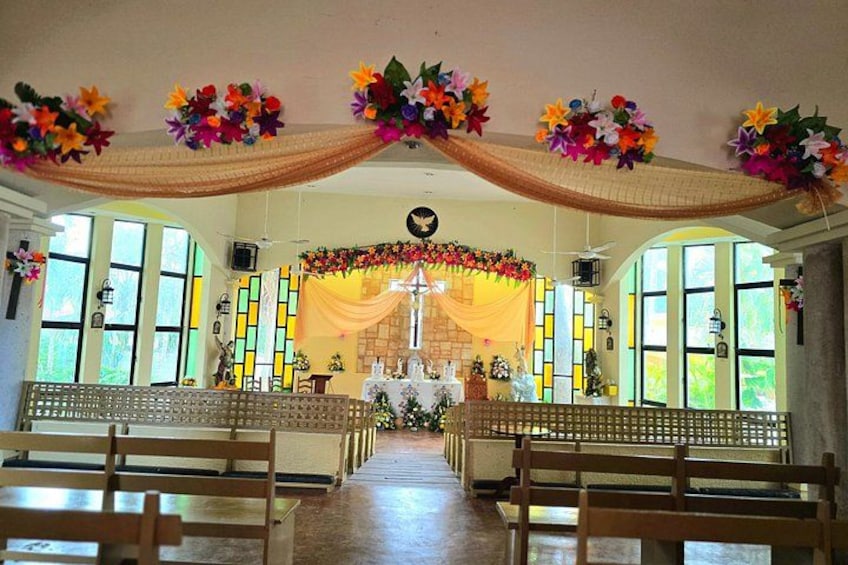 A church interior with pews, floral decorations, stained glass windows, and a central altar. 2