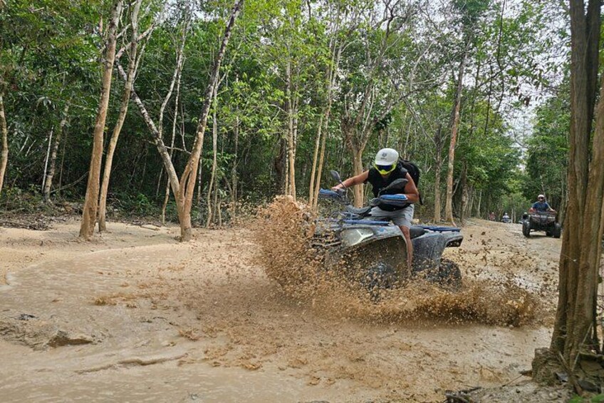 A person riding an ATV on a muddy path surrounded by trees. 1