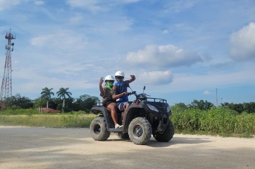 Two people on an ATV on a paved road with greenery and a communication tower in the background. 5
