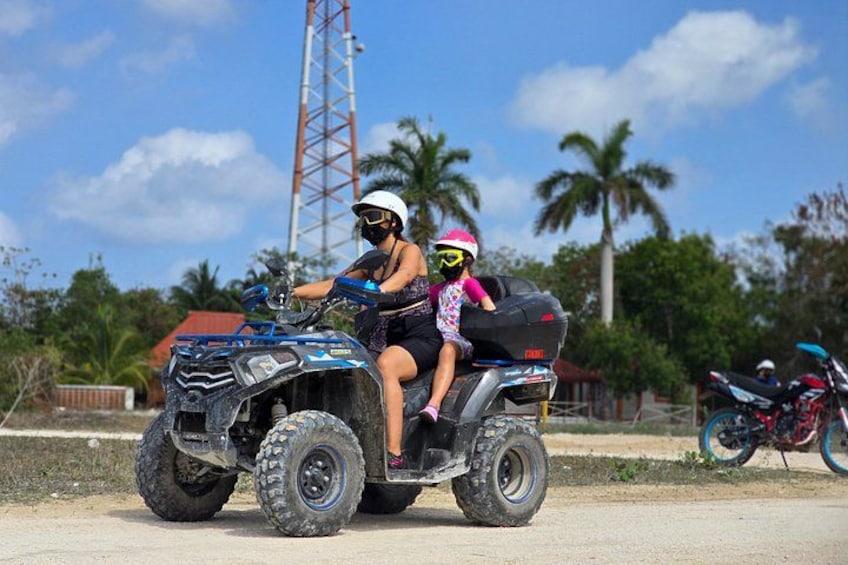 A quad bike with a passenger, a red building, and palm trees in the background. 5