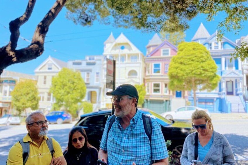 A group of people standing on a street with Victorian-style houses in the background. 3