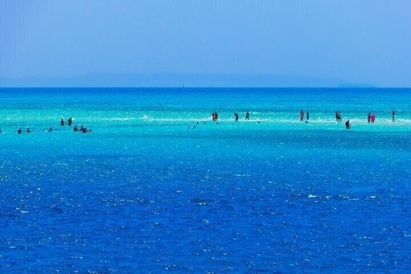 A beach with clear turquoise water and people swimming and sunbathing. 5
