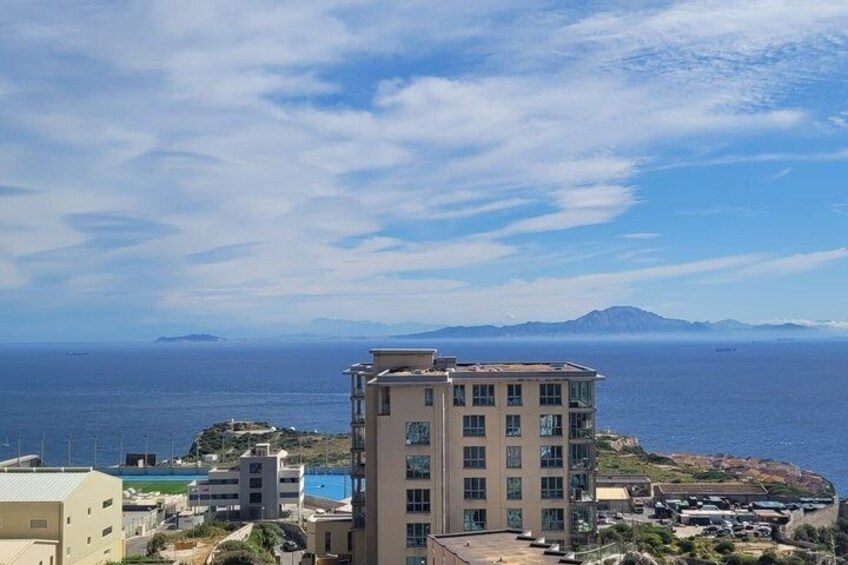 A coastal cityscape with a prominent building, a clear sky, and distant mountains. 4