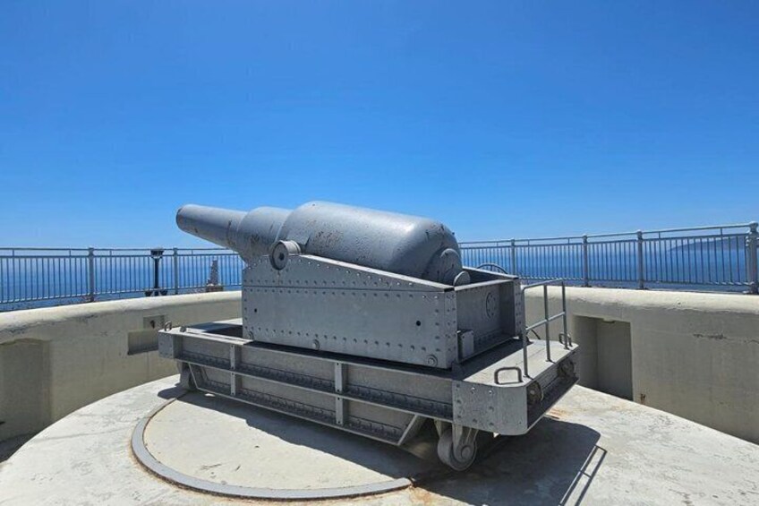 A large artillery piece mounted on a concrete platform with a railing in the background. 3
