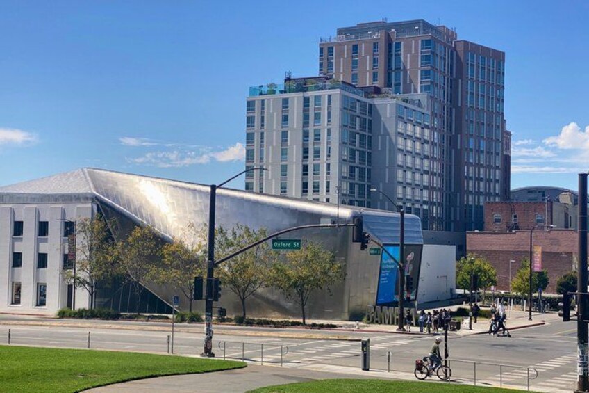 A modern building with a unique angular design, a street with a traffic light, and a cyclist in the foreground. 2
