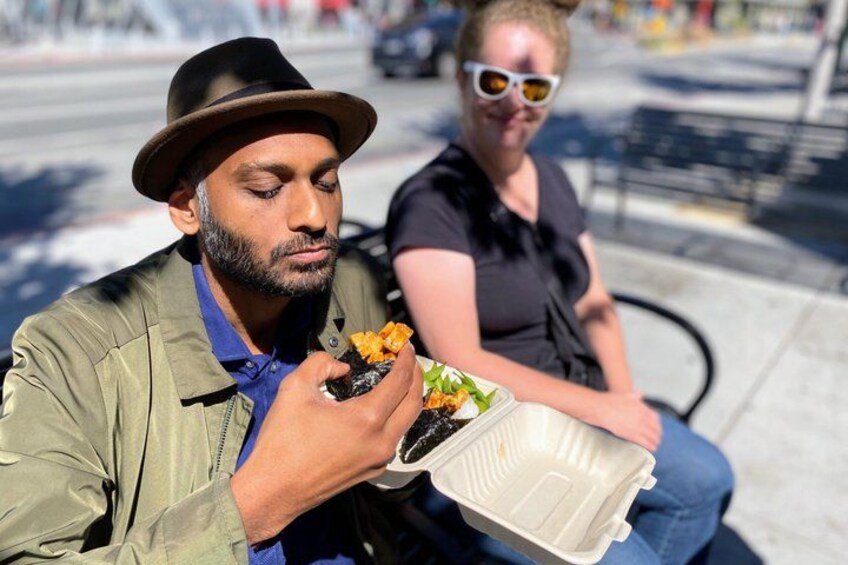 A person sitting on a bench eating food from a takeout container. 1