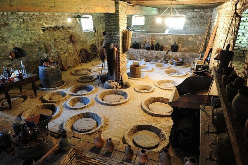 A traditional kitchen with stone walls, wooden barrels, and circular stone basins. 2