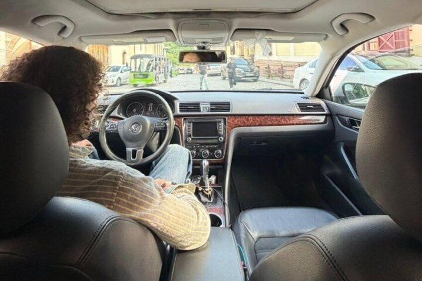 A person driving a car with a steering wheel, dashboard, and leather seats. 2