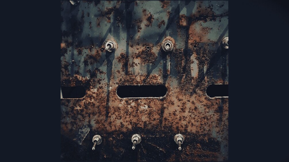 A rusted metal surface with bolts and rectangular cutouts. 2
