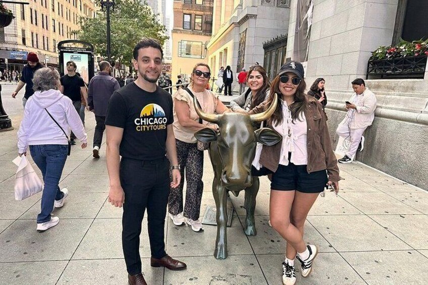 A group of people posing with a bull statue in an urban setting. 2