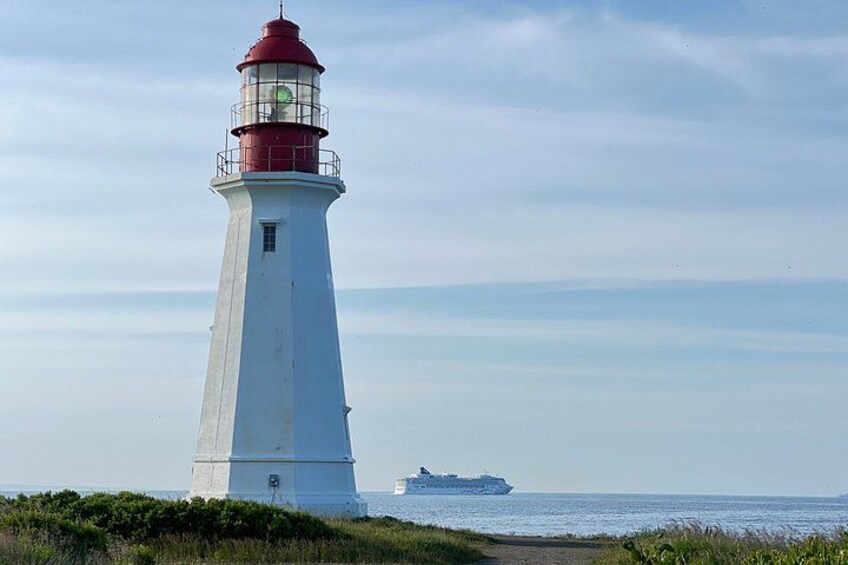 A white lighthouse with a red top, a ship in the distance, and a clear sky. 3