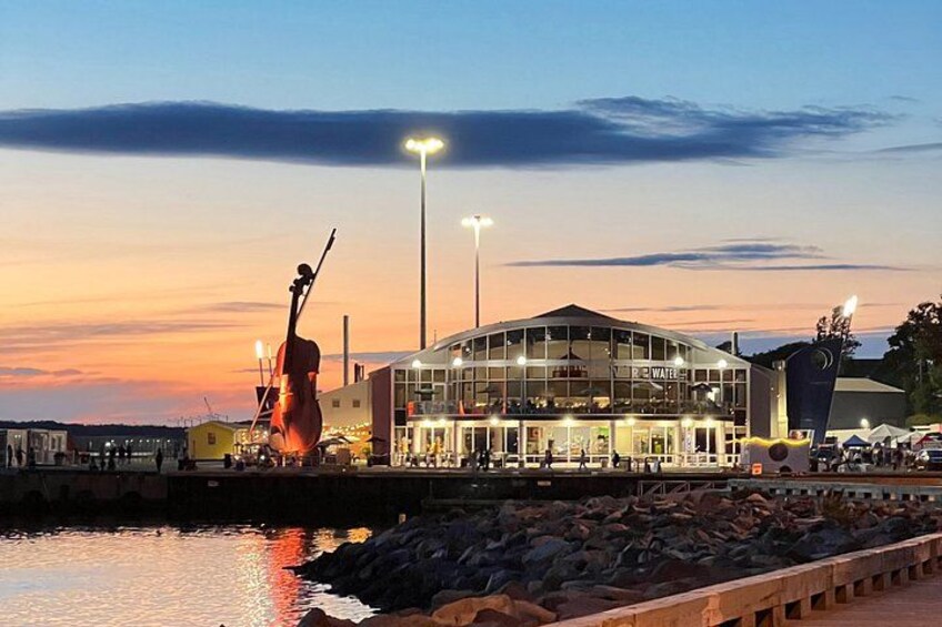 A waterfront building with a violin sculpture, a glass facade, and a sunset sky. 2