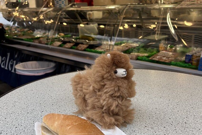 A plush toy llama on a table with a baguette in front of it. 3