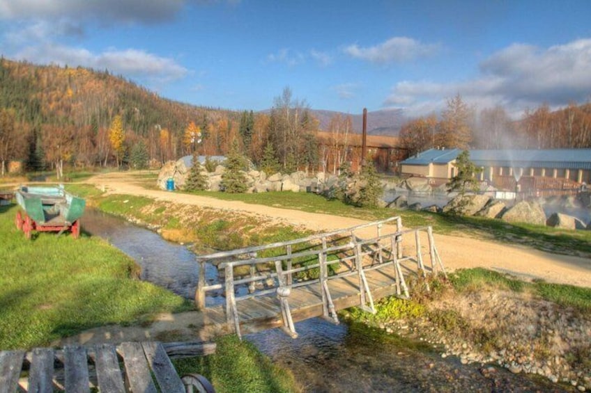 A wooden bridge over a stream, a boat, a forested hillside, and a building with a chimney. 3